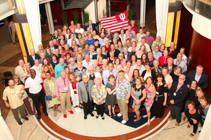A large group of IU School of Dentistry alumni with an IU flag gathered in a lobby.